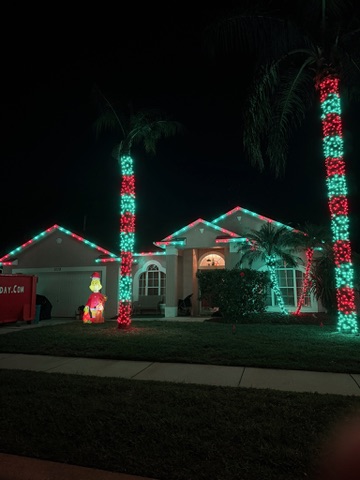 Red and green Christmas lights outlining a Florida home and wrapping its palm trees